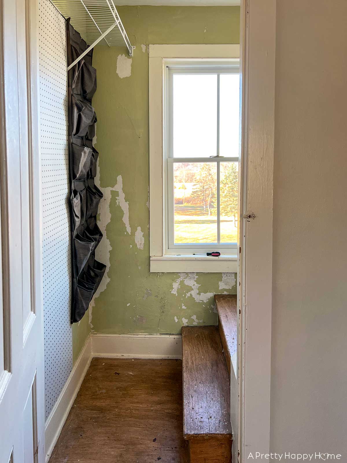 Before photo of an attic stairwell with peeling lime green paint, wire shelving, peg board, and a shoe rack.