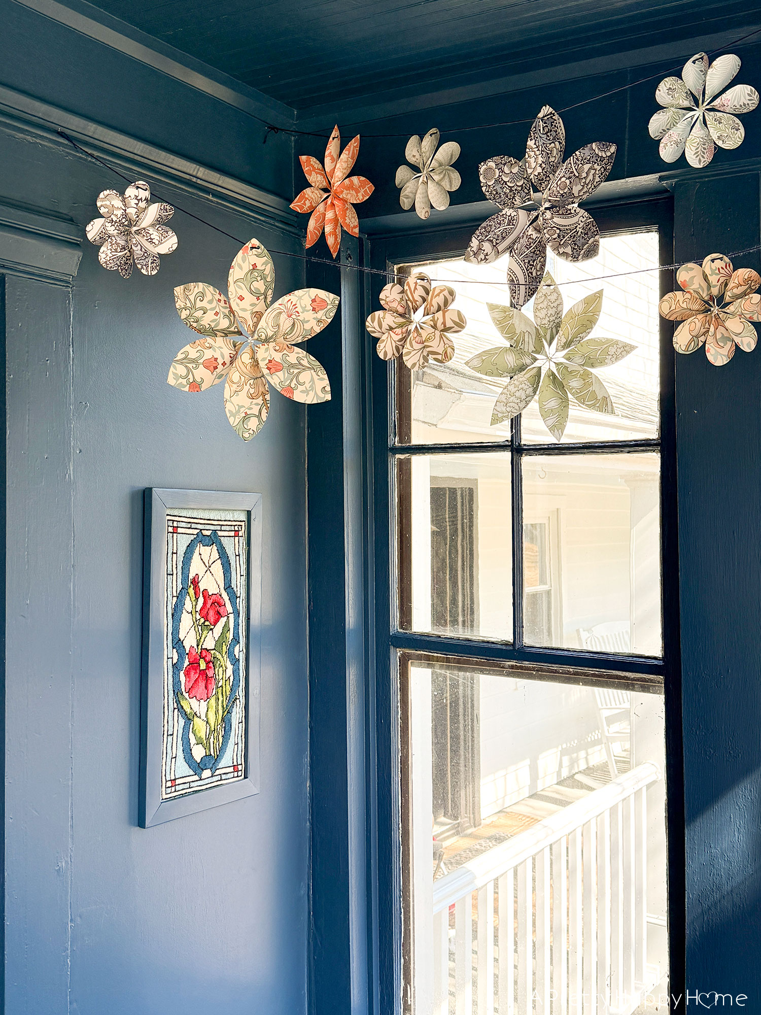 scrapbook paper flower garland hanging over a navy blue sunporch and blooming geraniums spring party decor wedding shower decor 