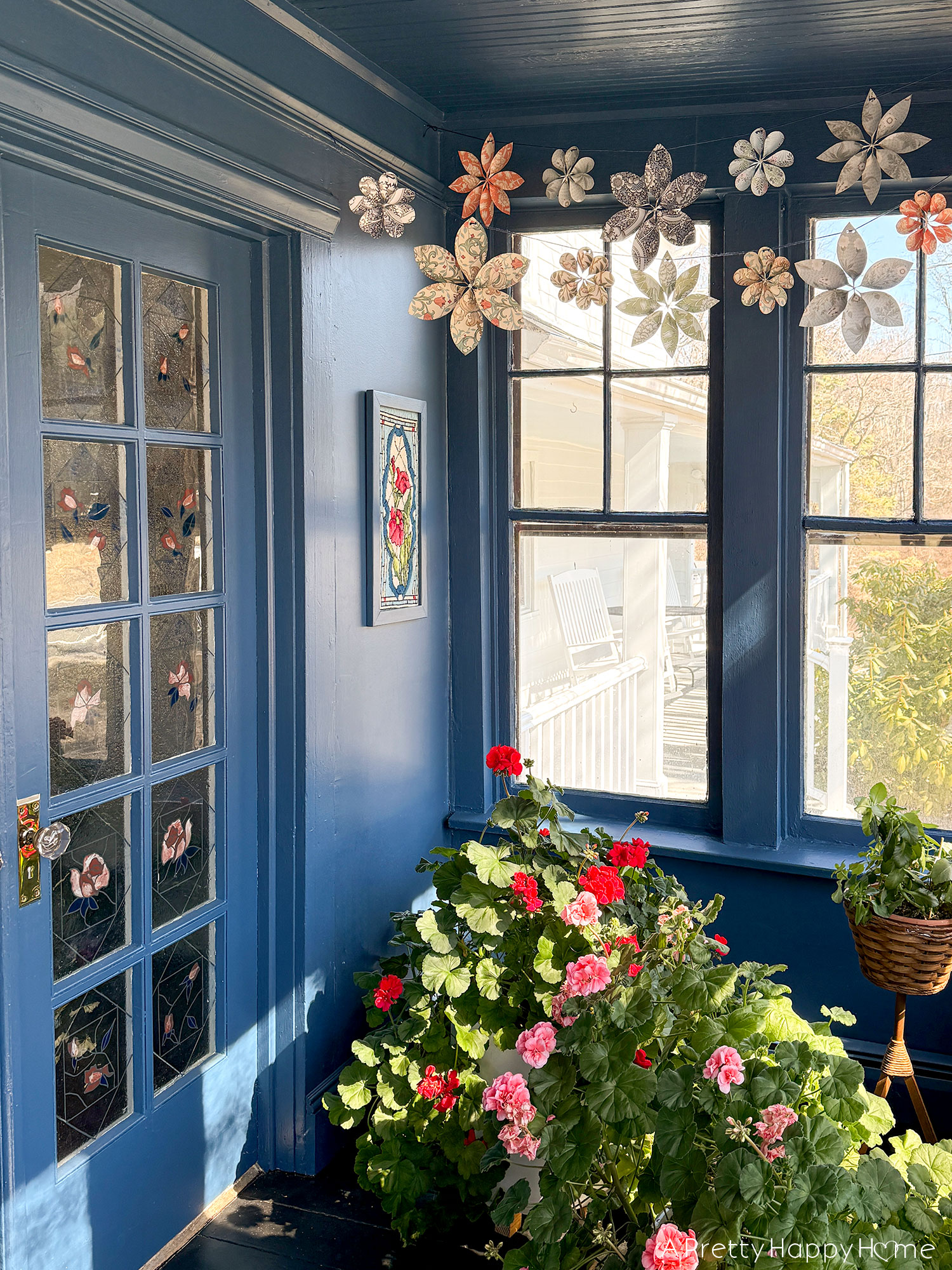 scrapbook paper flower garland hanging over a navy blue sunporch and blooming geraniums spring party decor wedding shower decor 