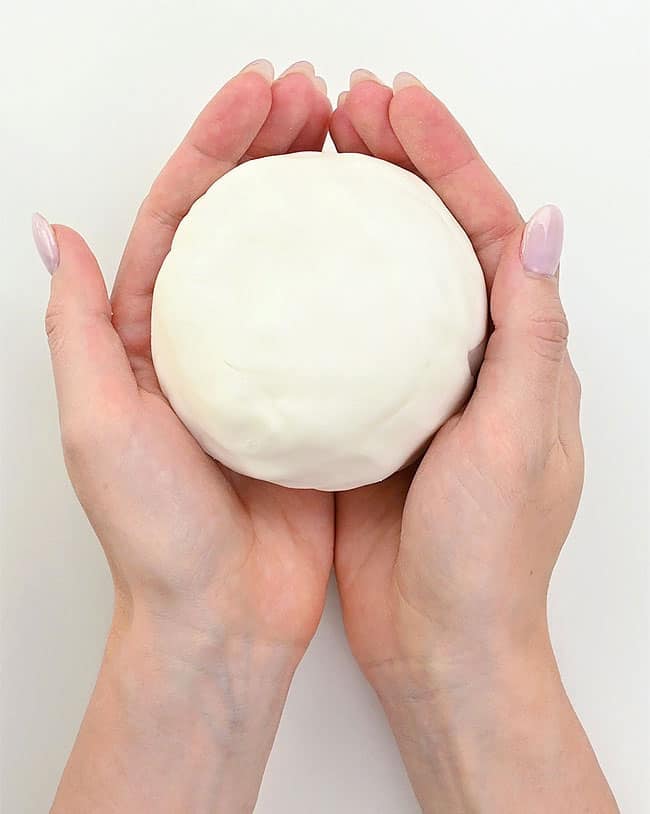 two hands holding a ball of white clay, which is homemade air dry clay you can make with basic kitchen ingredients. recipe is from one little project and shown here on the happy list.