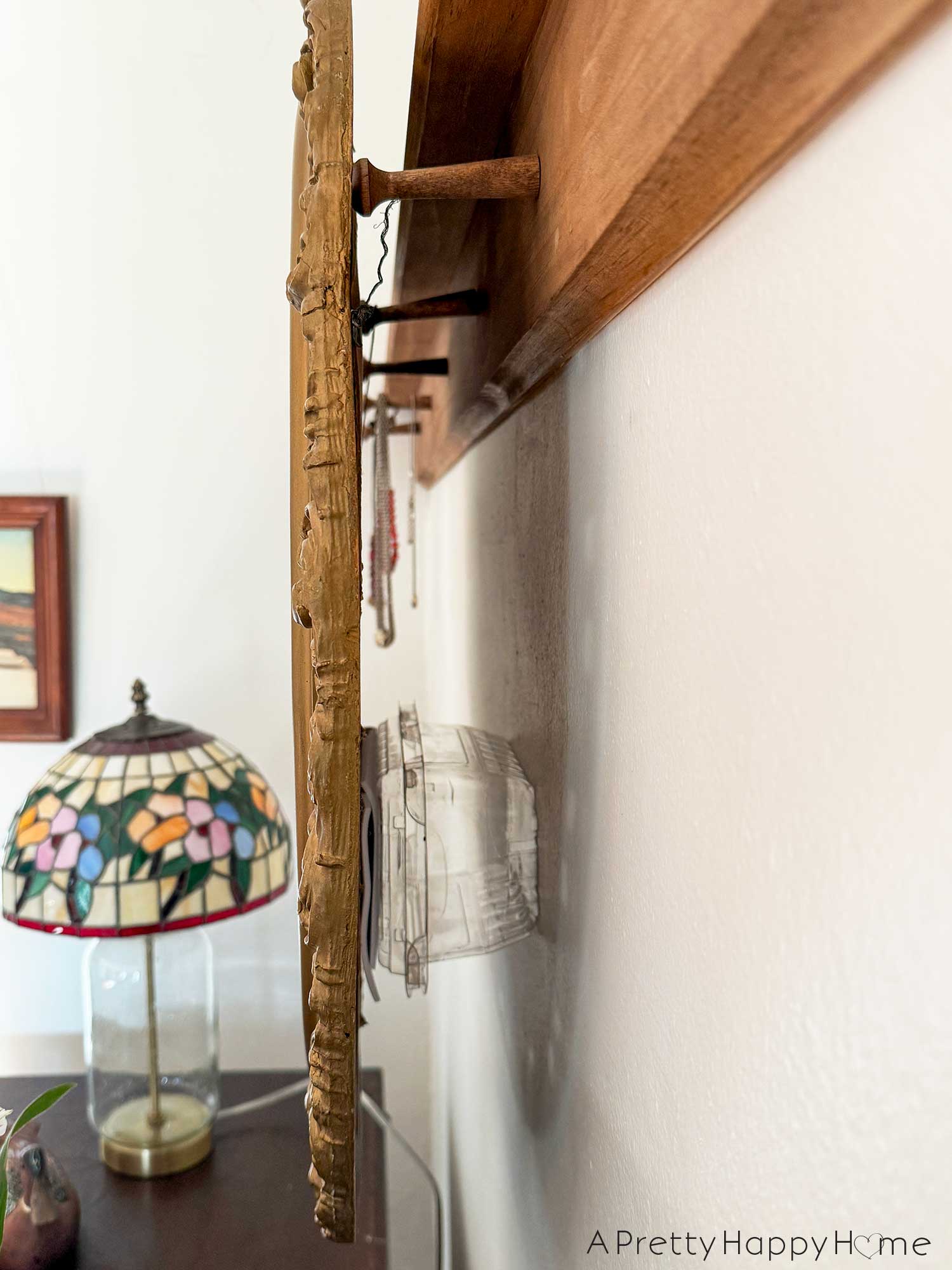 how to hang a mirror from a peg rail. Picture shows the hanging wire on the back of an ornate mirror hanging over 3 of the wood pegs on the rail. there's a clear plastic strawberry container used as blocking behind the mirror to hold it parallel to the wall. 