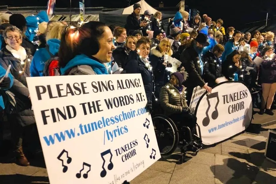 group of people from a tuneless choir holding a sign inviting people to sing with them. shown here on the happy list.