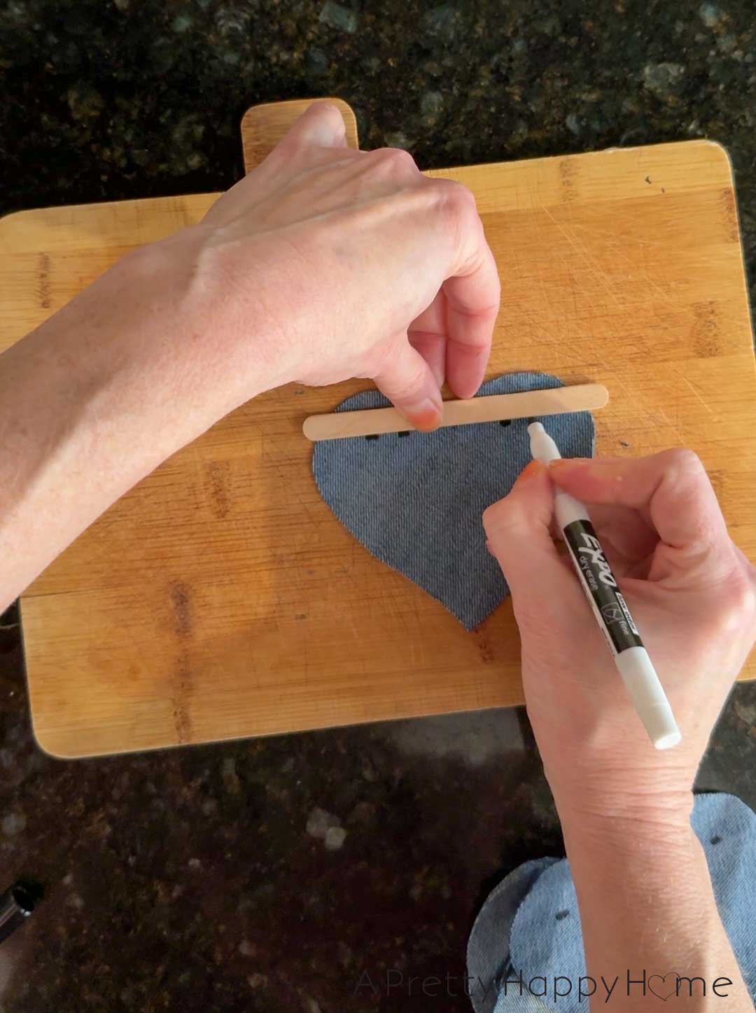 two hands marking lines on the back of a denim heart with a marker and a straight edge to know where to cut to hang the denim heart on a banner or bunting line