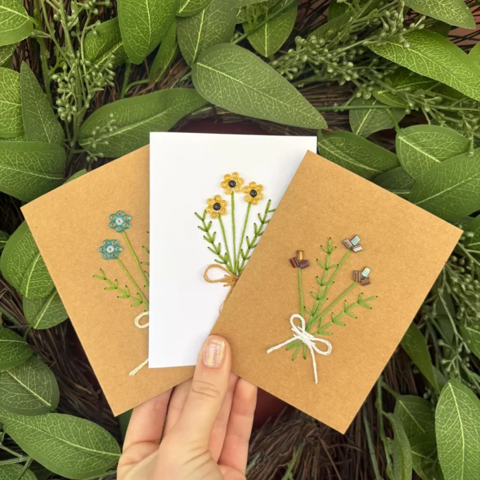 set of three handmade embroidered greeting cards on white or brown paper. The embroidery is a set of 3 flowers tied with a ribbon from etsy shop twistedwoodshandmade 