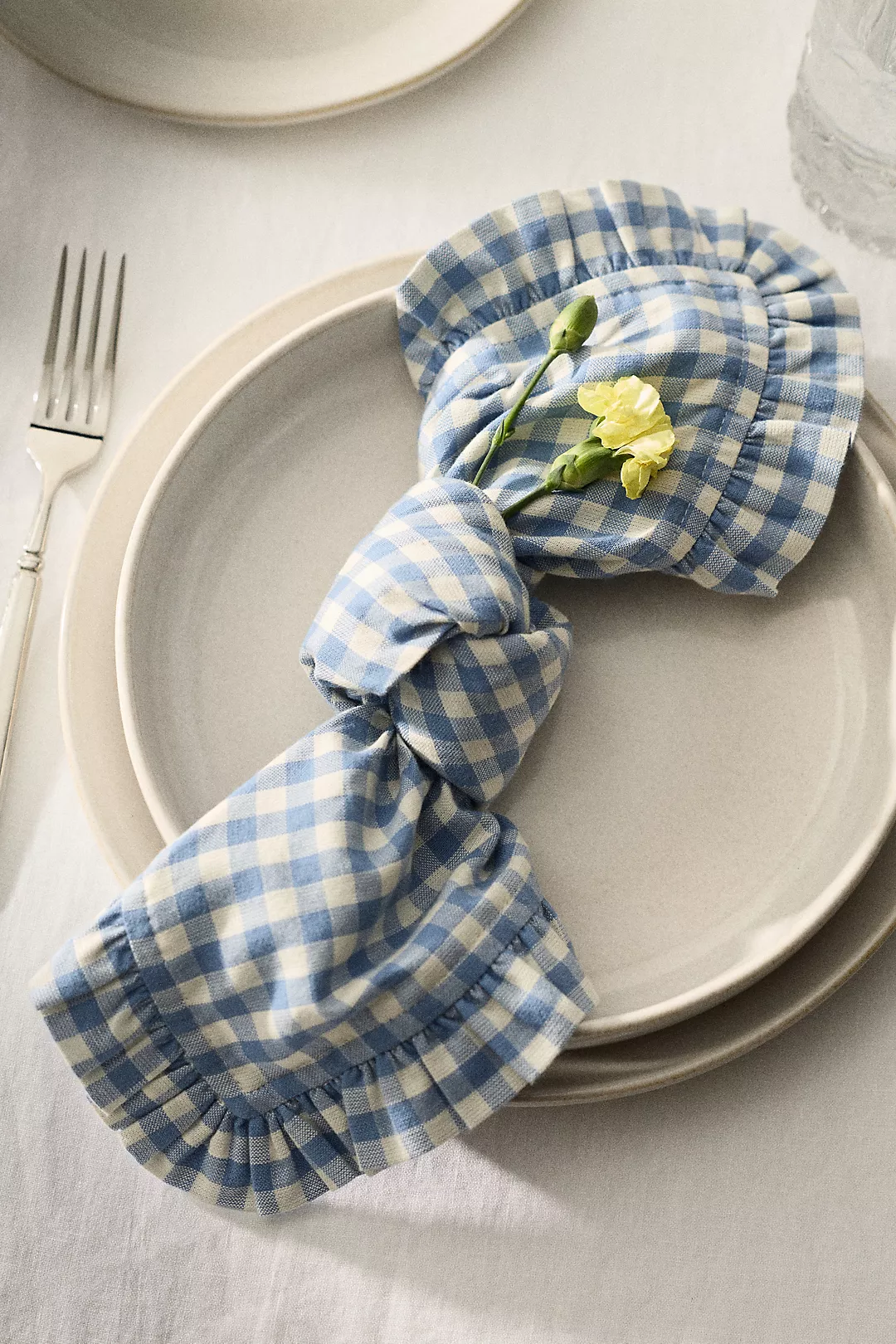 blue gingham ruffled cloth napkin tied in a knot with two flowers tucked into it