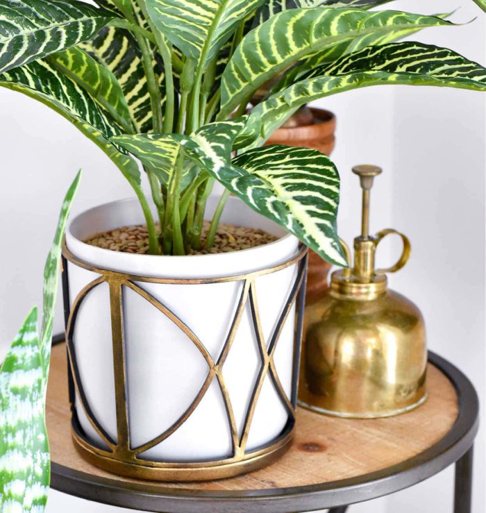 the decorative metal part from a glass light shade upcycled into a decorative holder for a plain white planter with a green plant inside. Idea from Sadie Seasongoods.