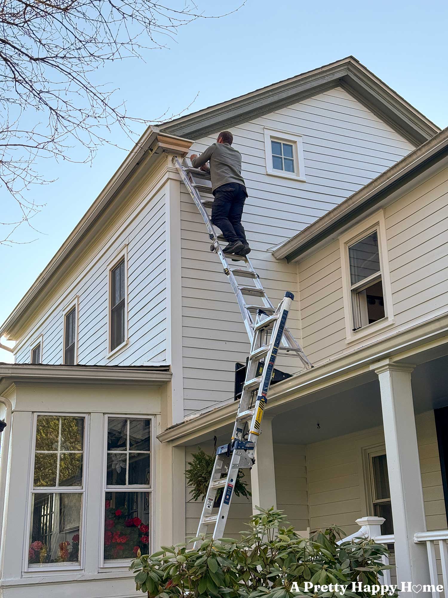 Man standing on ladder fixing a gable return on a greek revival home painted white