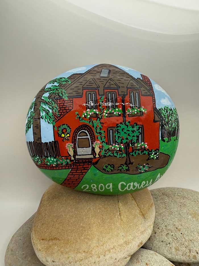 custom house portrait on a river rock showing a hand painted red house surrounded be trees and grass 