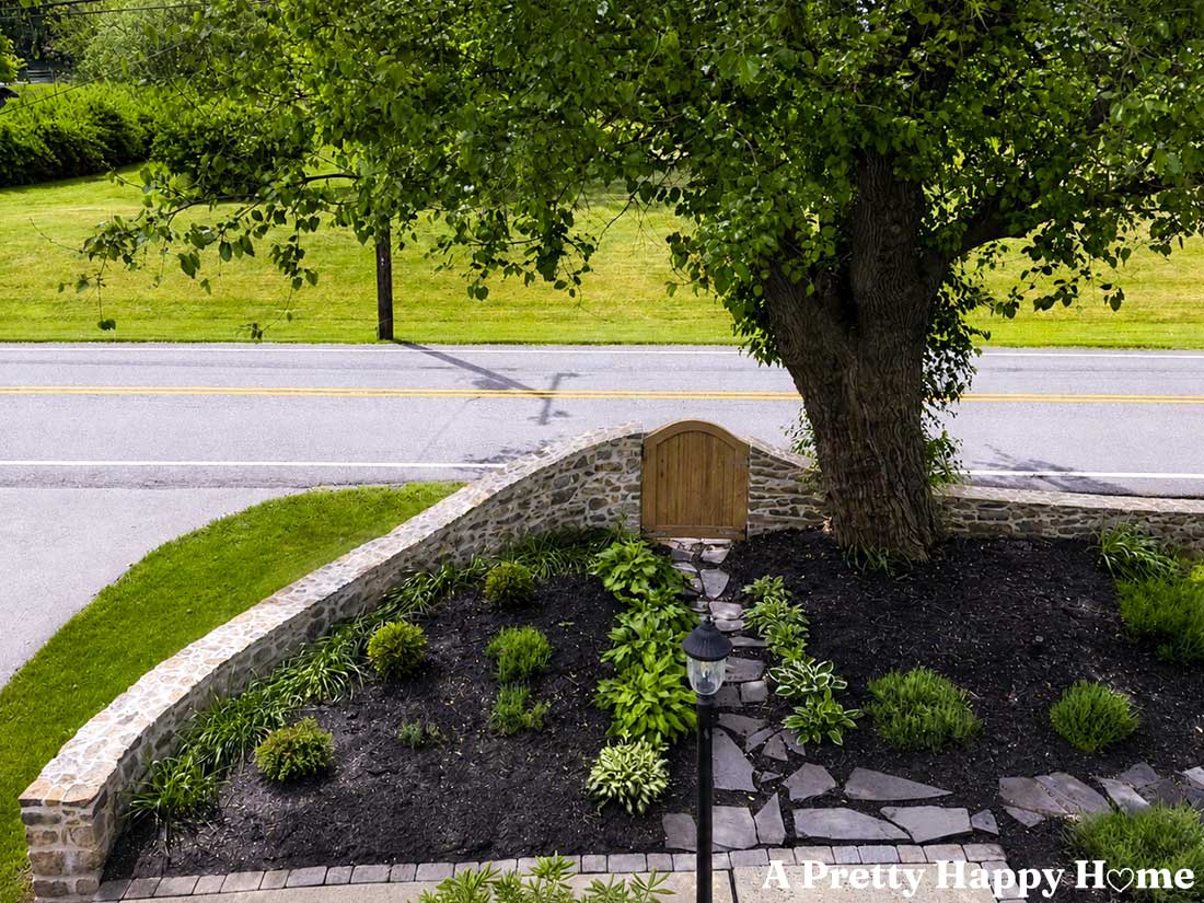 AI generated image of a curved and sloped stone wall with a wood gate that encloses a flower bed area